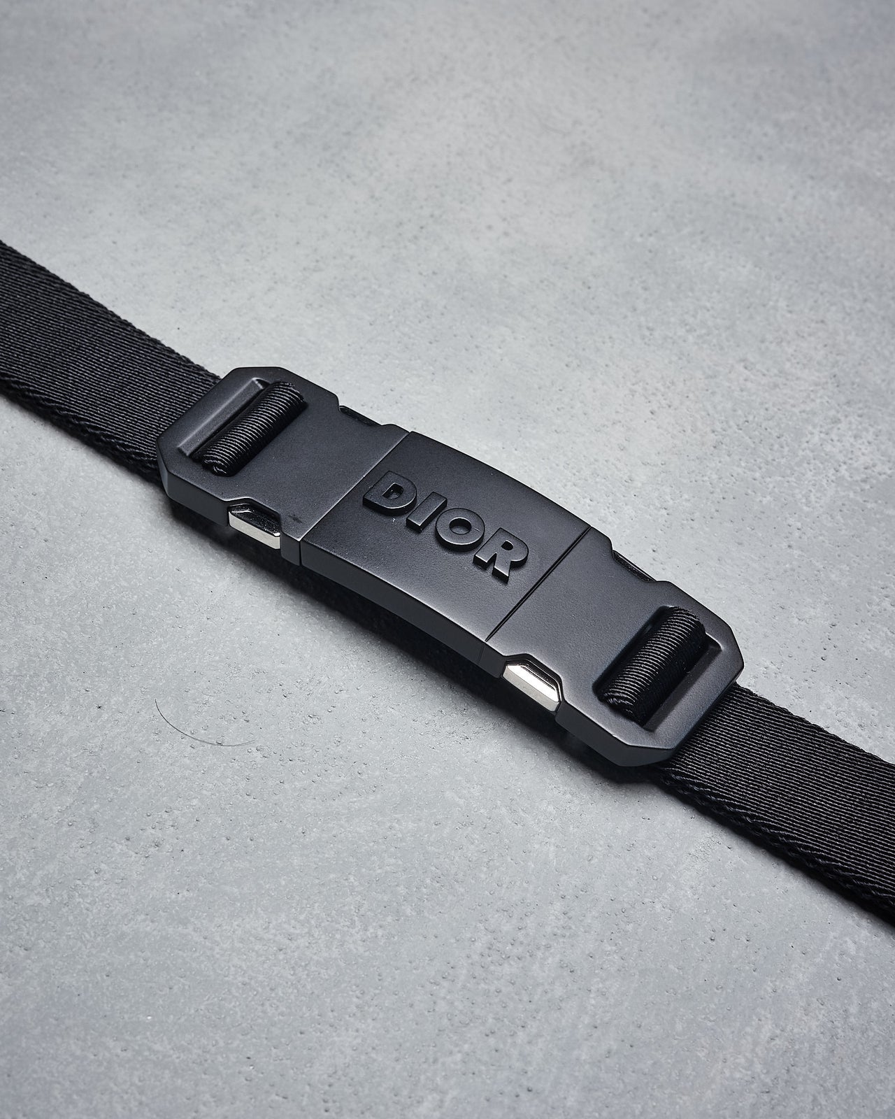 A black Dior belt with a metal buckle featuring the Dior logo, designed for men.