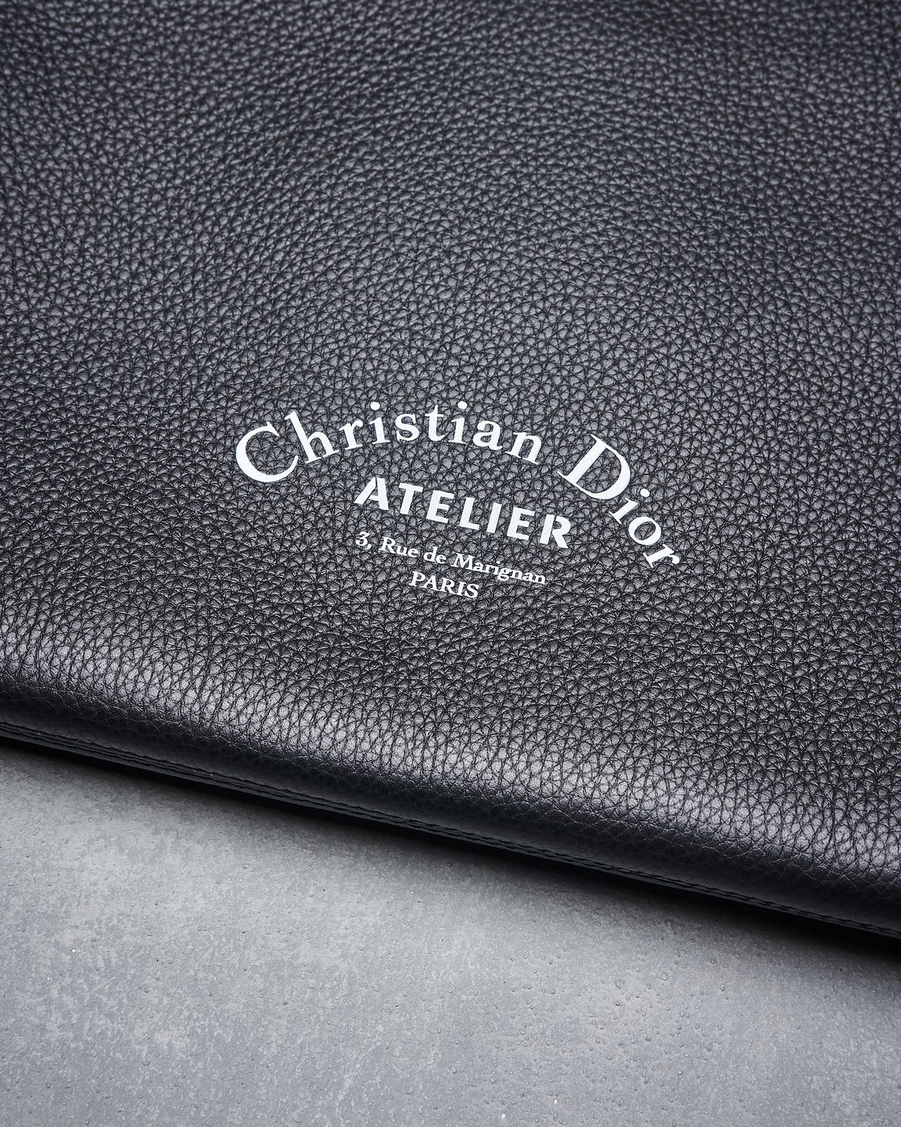 Black Dior Homme Atelier portfolio zip clutch with the brand's logo embossed on the front, made of satin bovine leather, closed with a zip and leather string.