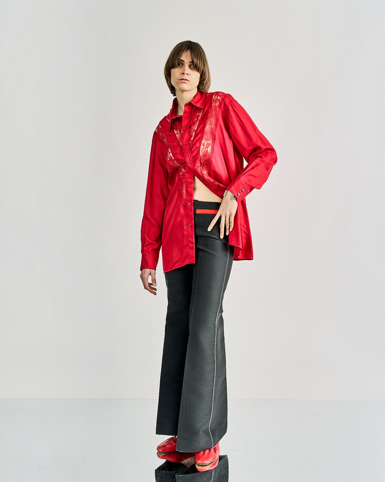 A model walks a Celine runway wearing an oversized khaki jacket over a red blouse and high-waisted beige trousers. The audience, seated on both sides, captures the show.