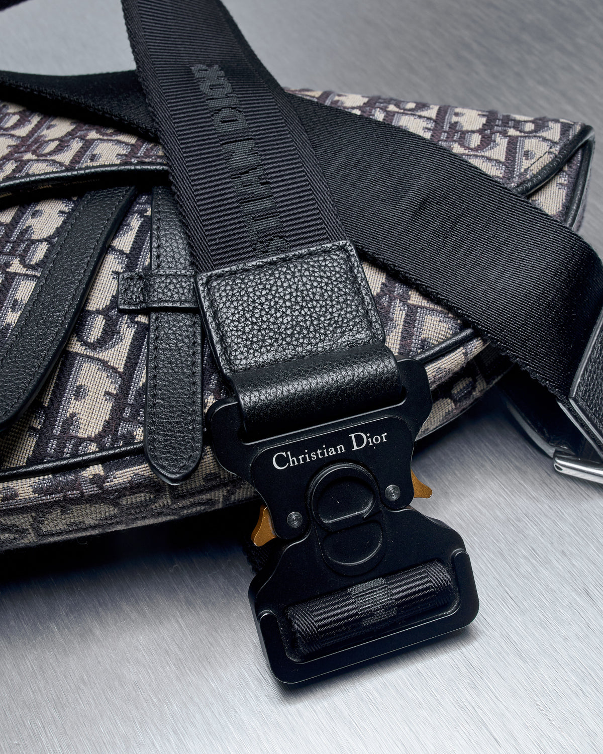 Designer crossbody saddle bag from Dior with intricate monogram pattern and sleek black adjustable strap. The curved flap closure adds elegance and modern appeal.