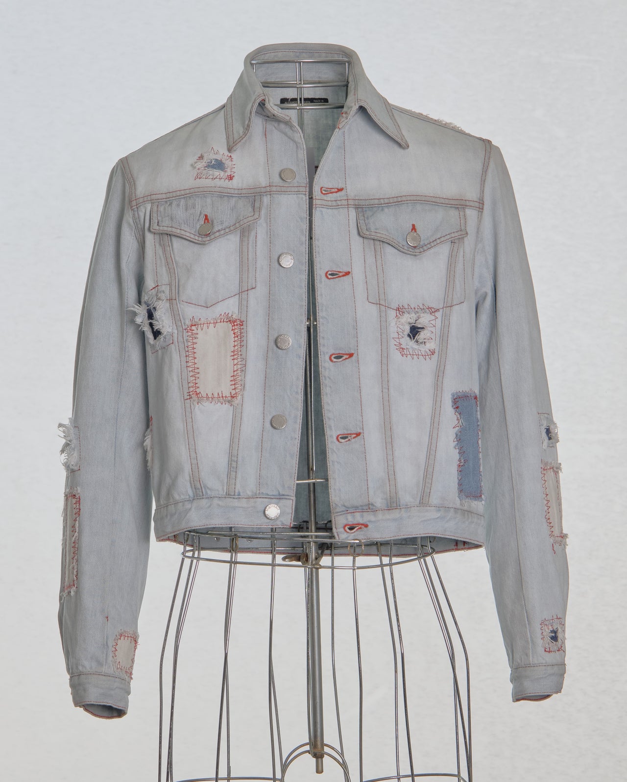 Denim Alexander McQueen jacket with patches on a mannequin against a light gray background