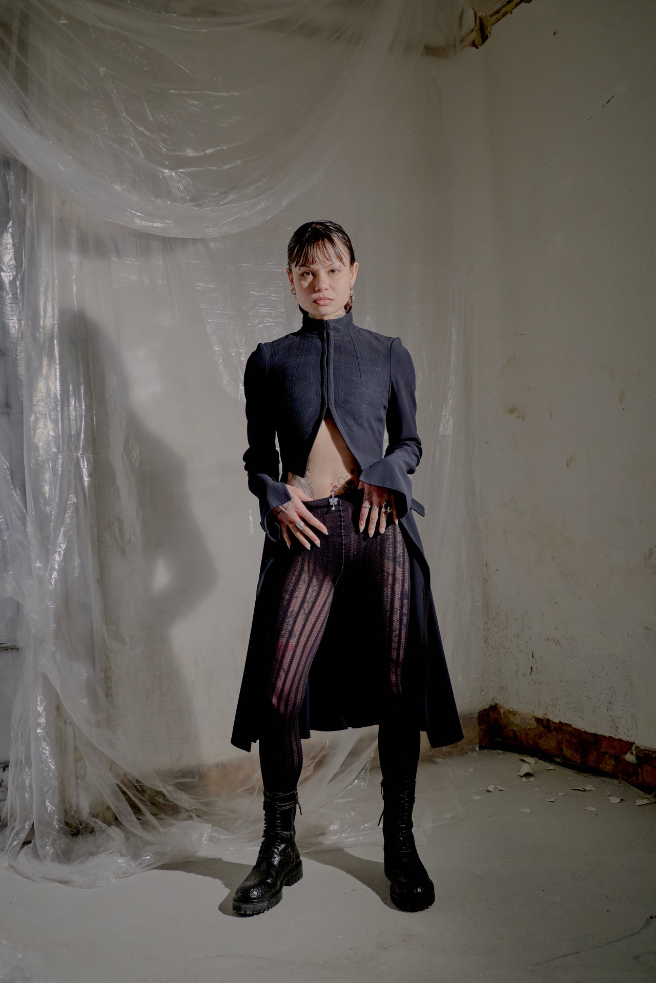 Person wearing a dark Alexander McQueen coat with striped pants in a minimalistic room.