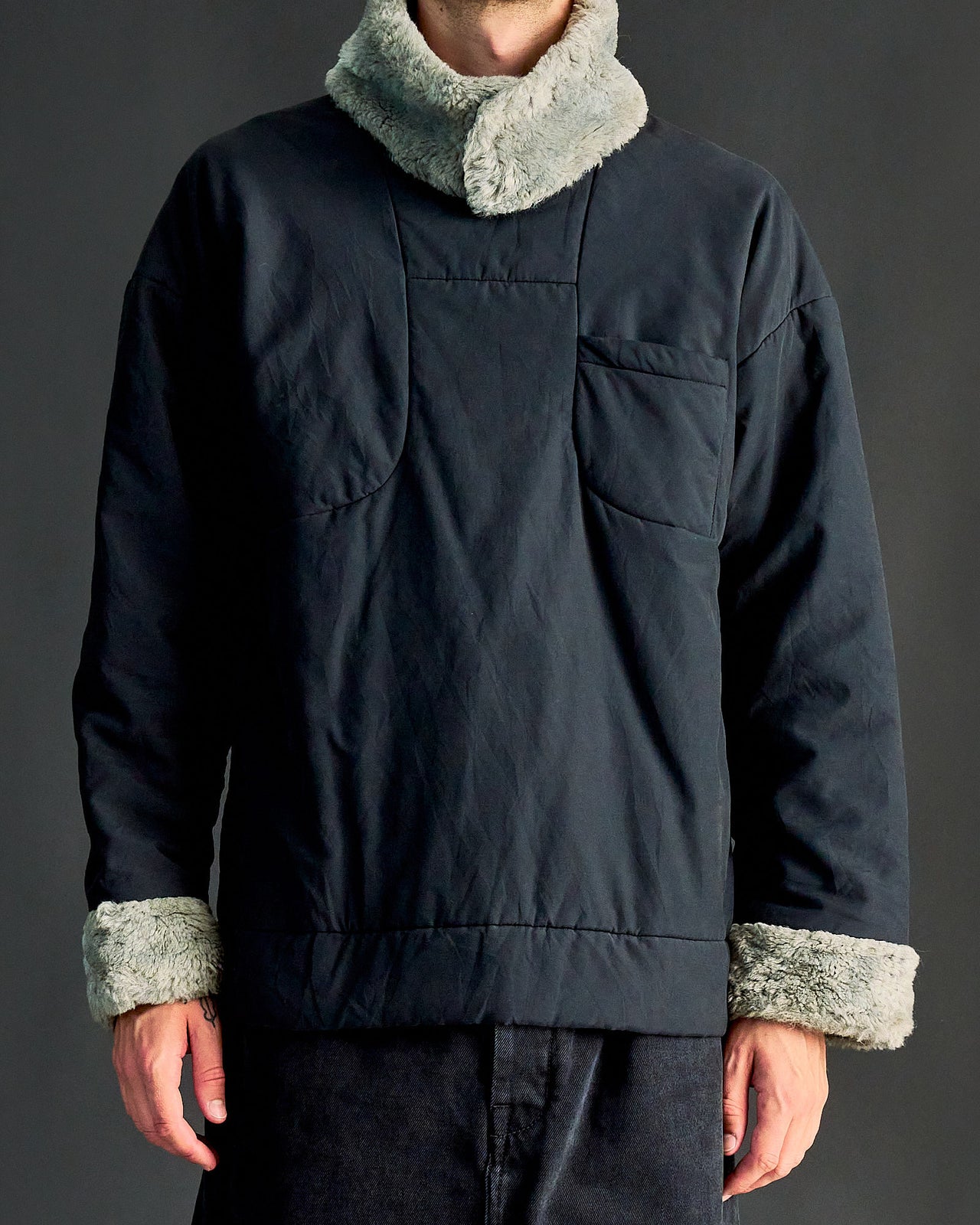 A person viewed from the back wearing a black Alexander Mcqueen shearling collar padded pullover with a visible external breast pocket.