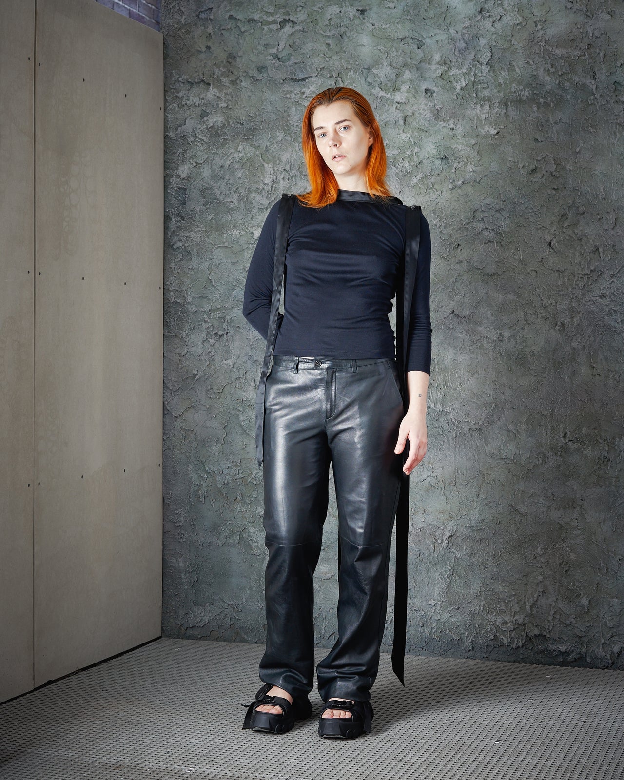 A model wearing a high-neck Alexander McQueen top with silk ribbon details on the collar and a draped open back, paired with trousers.