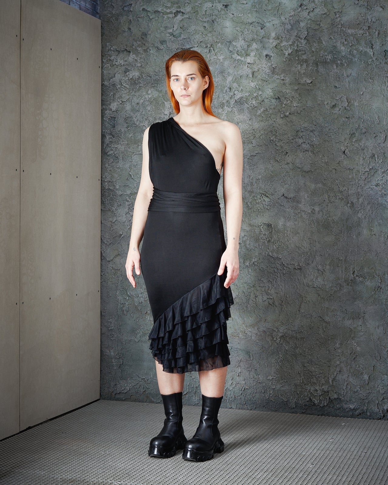 A model wearing a one-shoulder Alexander McQueen black dress with ruffle layers and a trailing fabric shoulder sash.