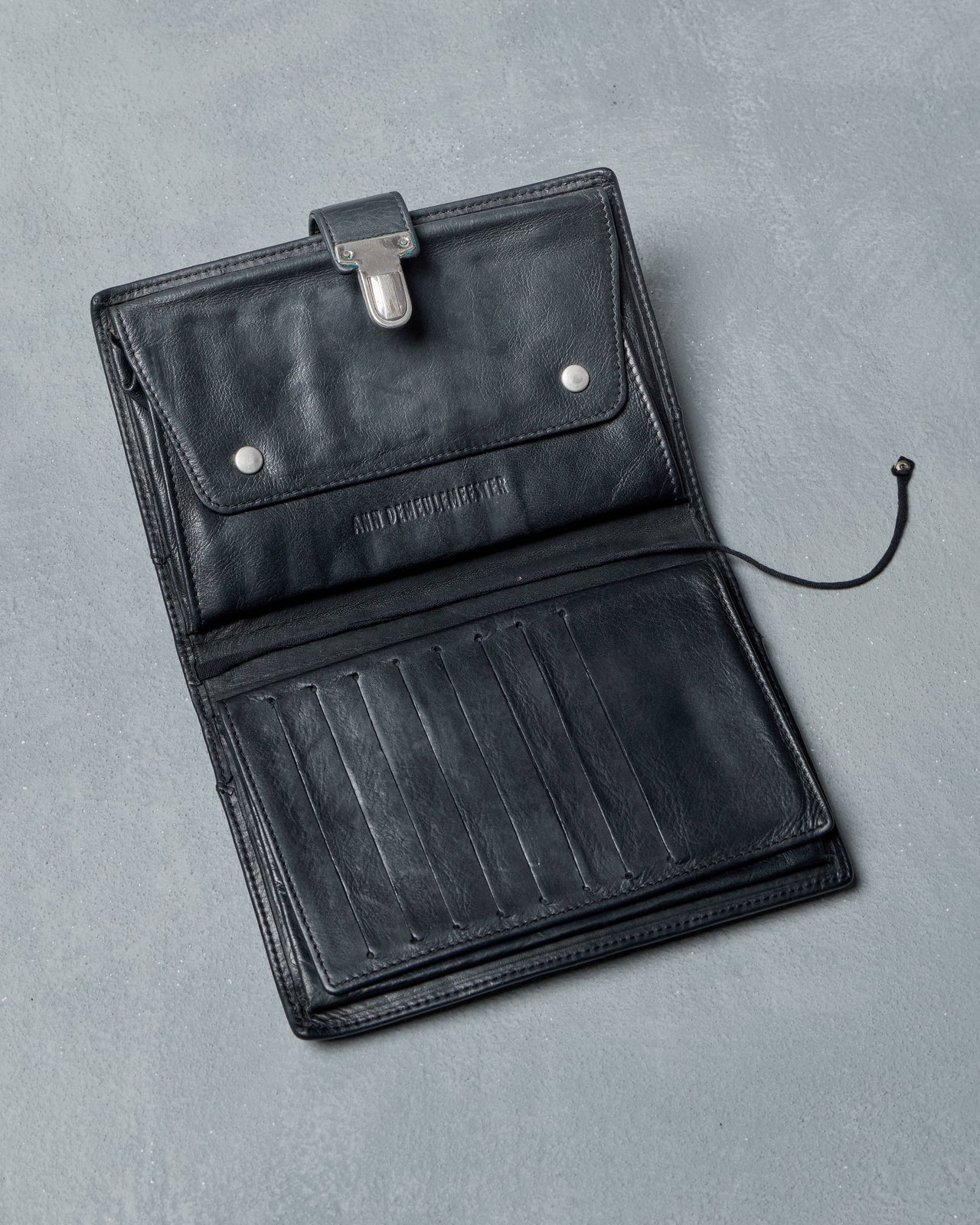 Black Ann Demeulemeester travel wallet with a silver clasp on a gray background