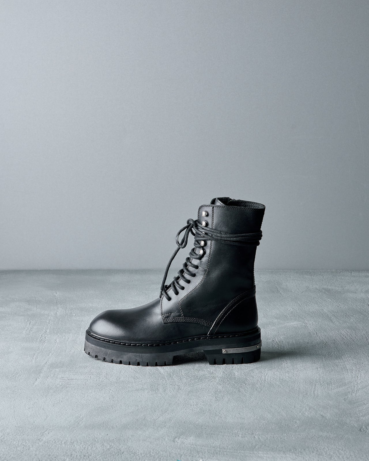 Black leather Ann Demeulemeester boot on a grey surface with a grey background