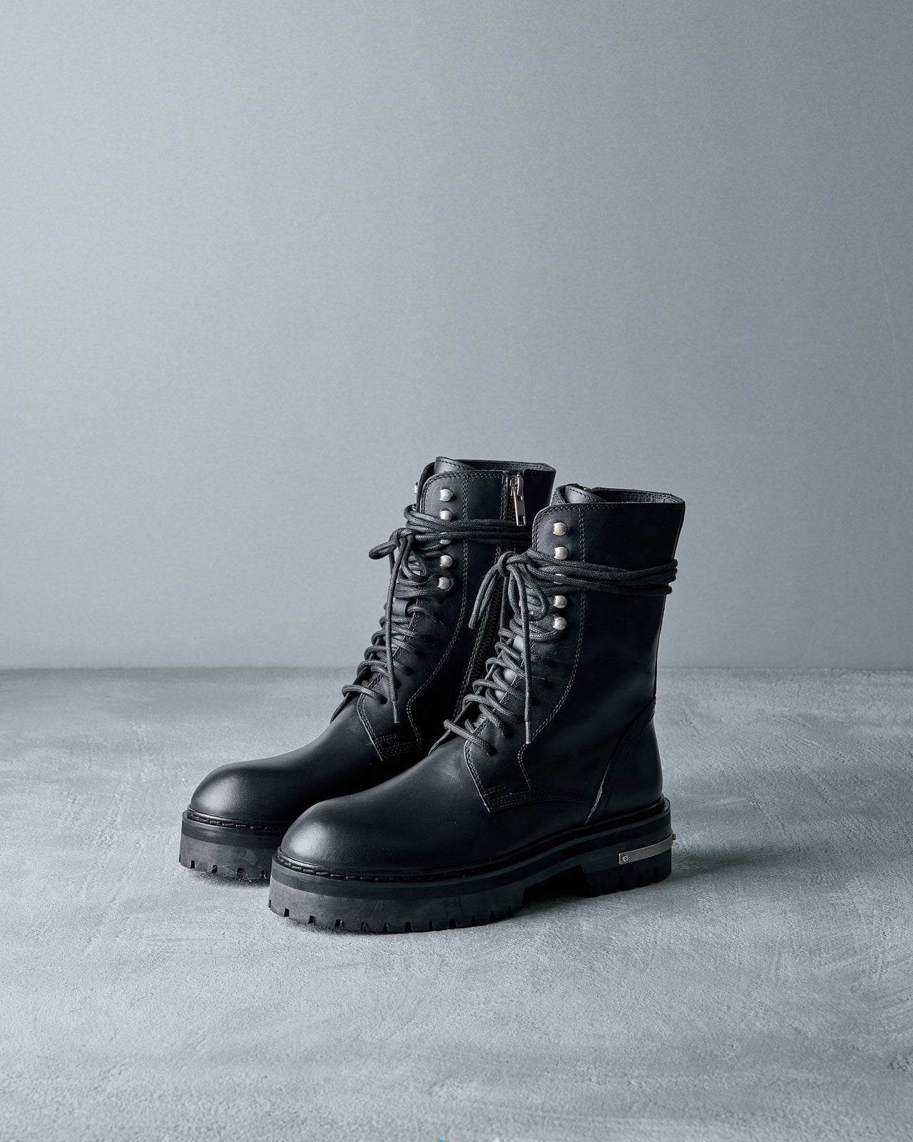 Black leather Ann Demeulemeester boot on a grey surface with a grey background