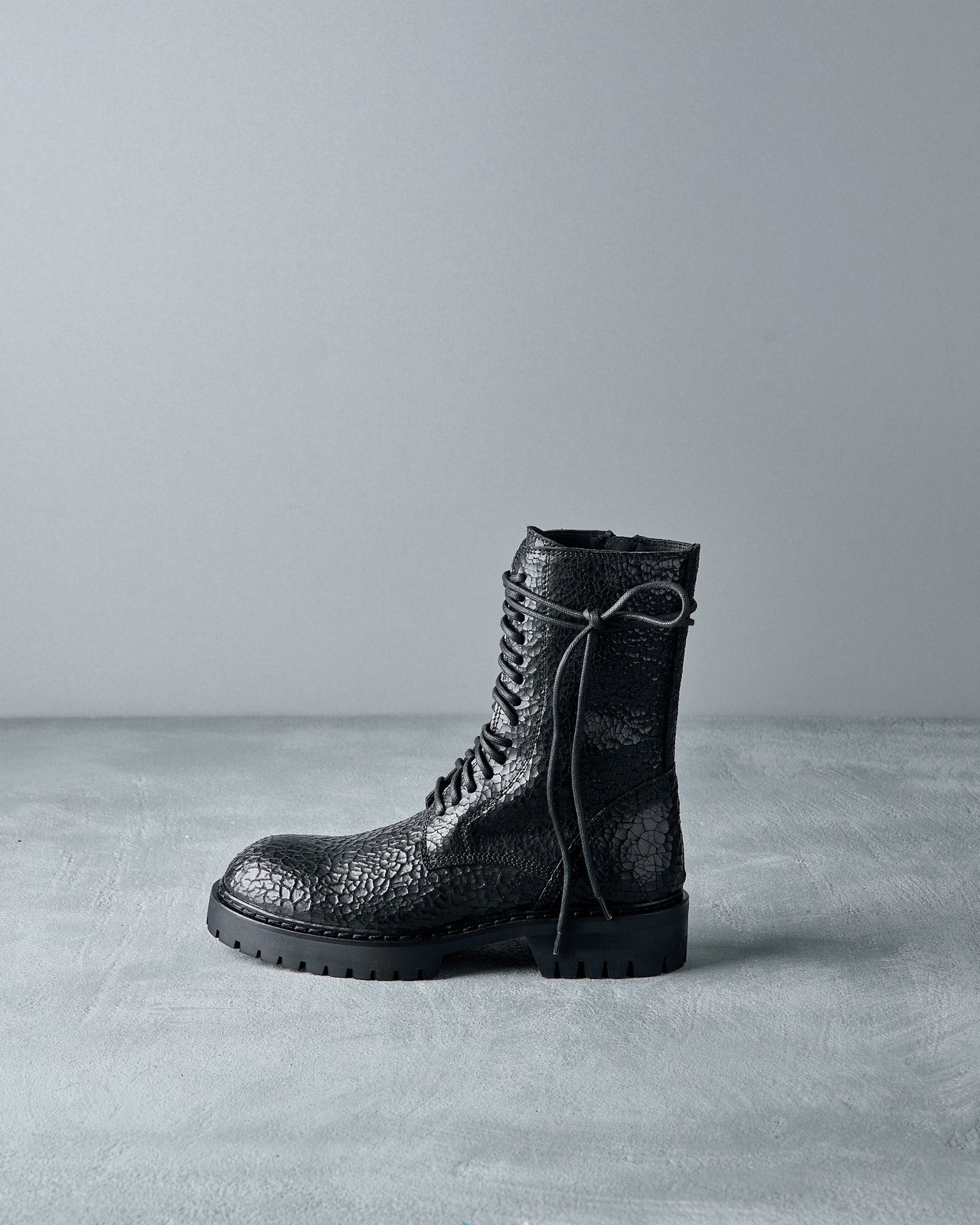 Black leather Ann Demeulemeester boot with textured sole on a gray background