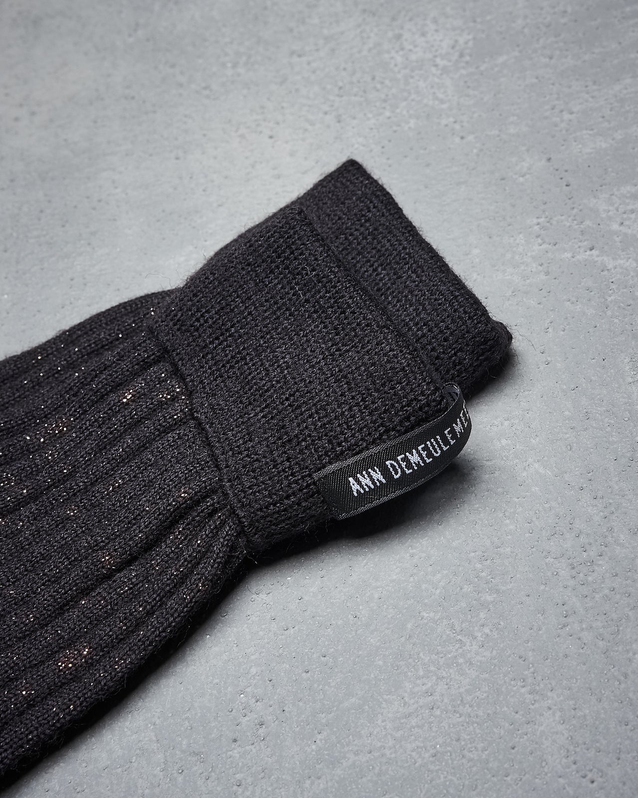 A pair of black metallic Ann Demeulemeester socks with a subtle pattern lie side by side on a gray textured background.