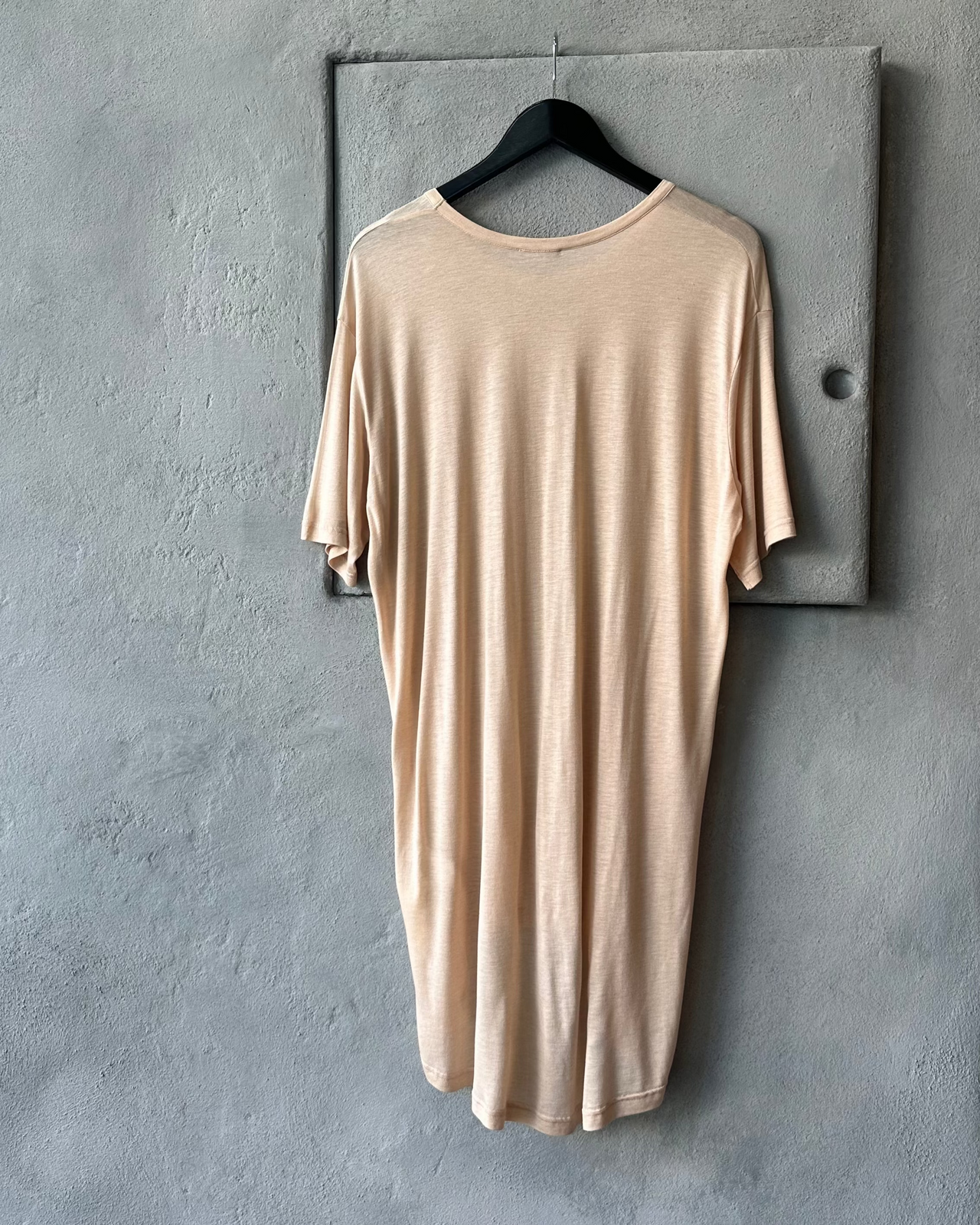 Beige Ann Demeulemeester top hanging on a hanger against a gray wall