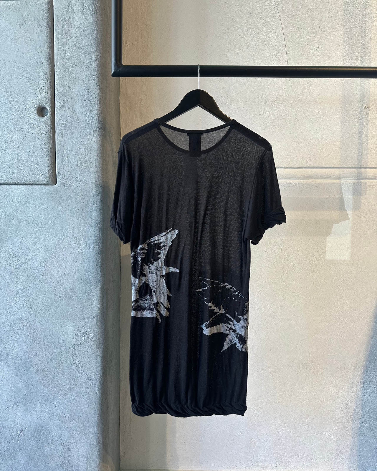 Black Ann Demeulemeester t-shirt with white butterfly designs on a hanger against a light gray wall.