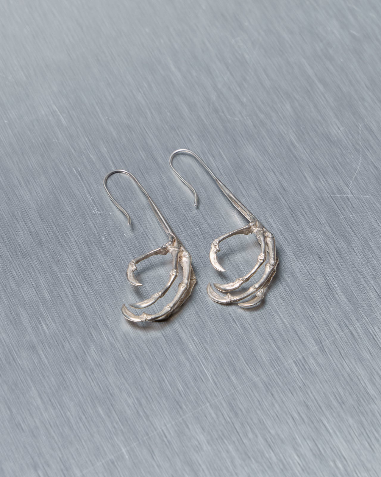 Pair of silver Ann Demeulemeester earrings on a gray background