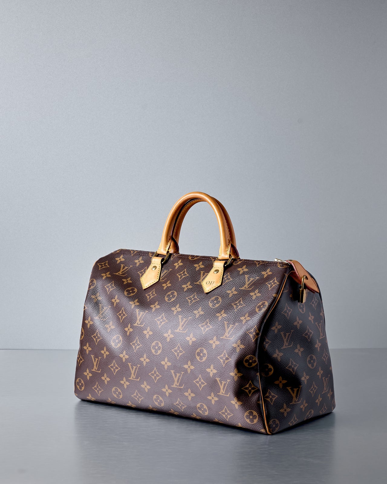 A brown Louis Vuitton Speedy 35 Monogram bag with tan leather detailing, displayed against a neutral background.