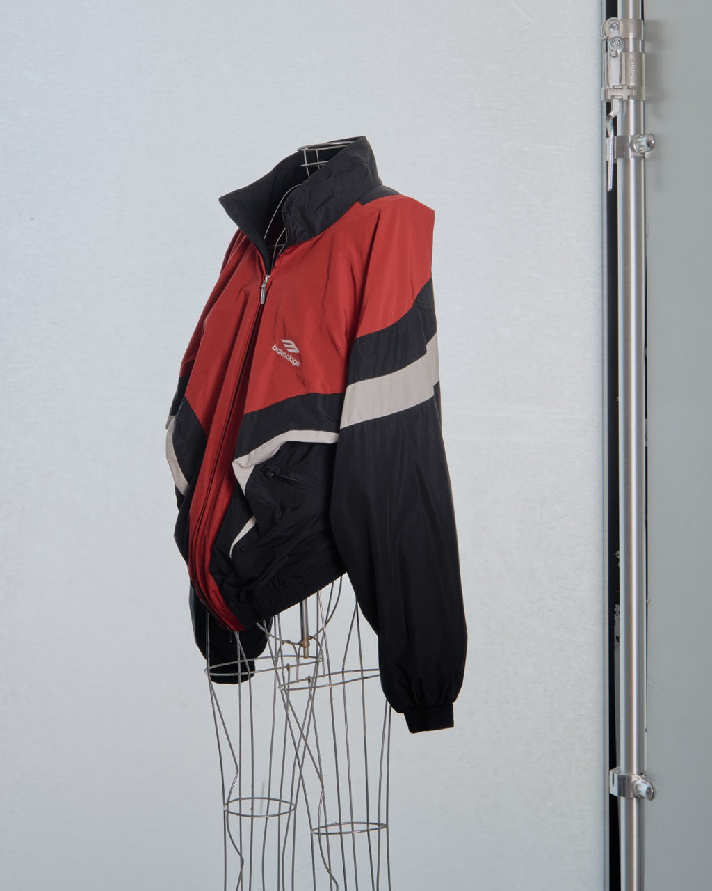 Red and black Balenciaga jacket with a logo on a mannequin against a light blue background