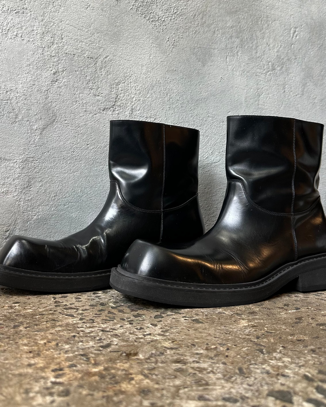 Black leather boot on a light gray surface with a concrete wall background