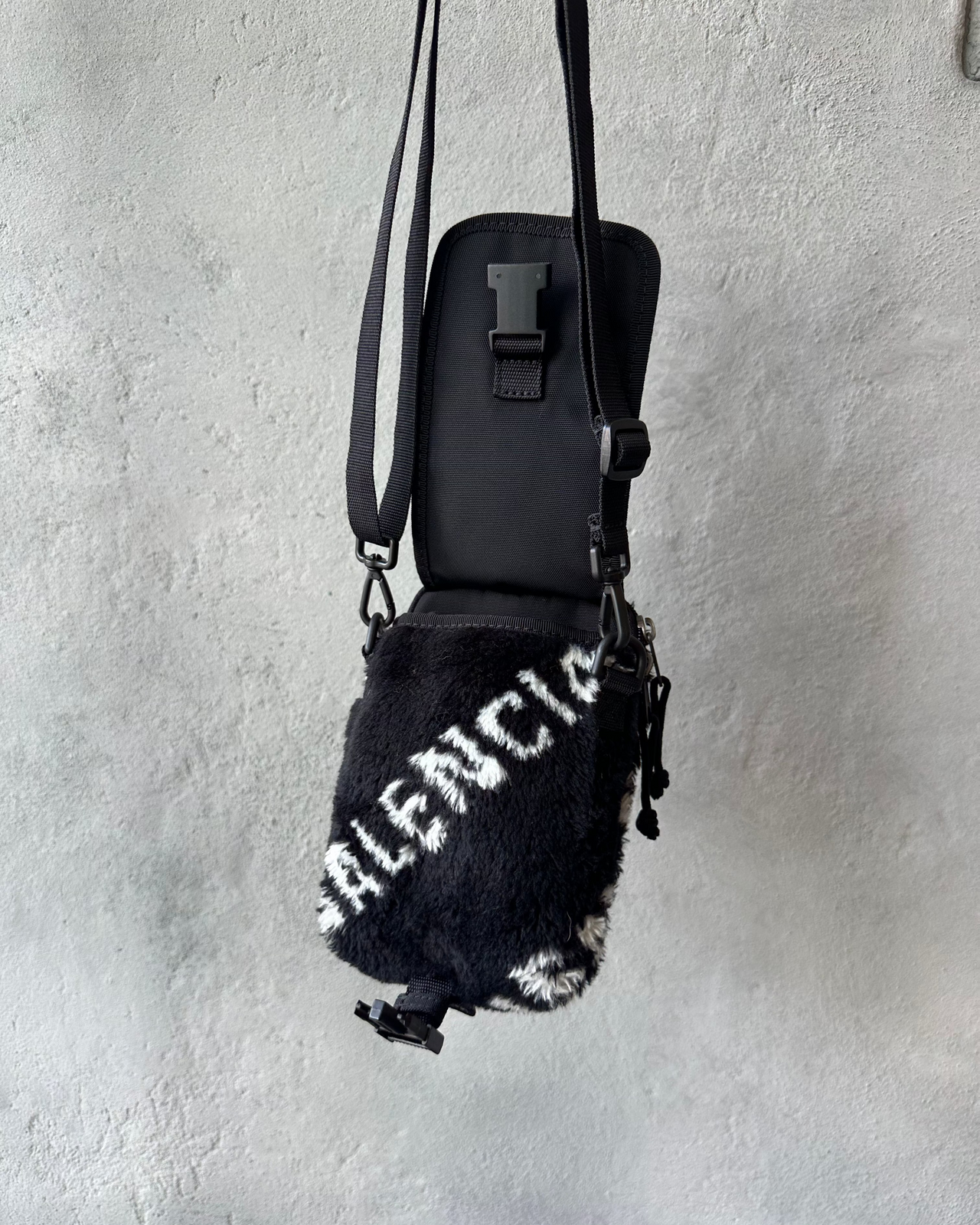 Small black Balenciaga bag with white text on a textured gray wall