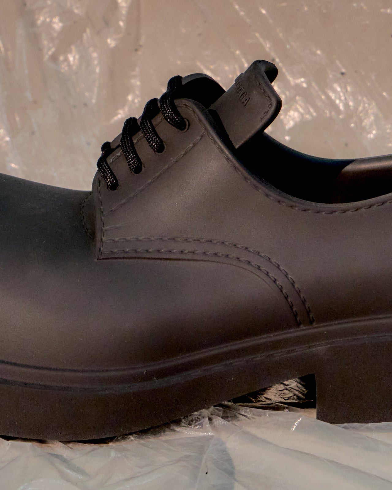 Black leather Balenciaga shoe on a light blue surface with a transparent plastic sheet in the background