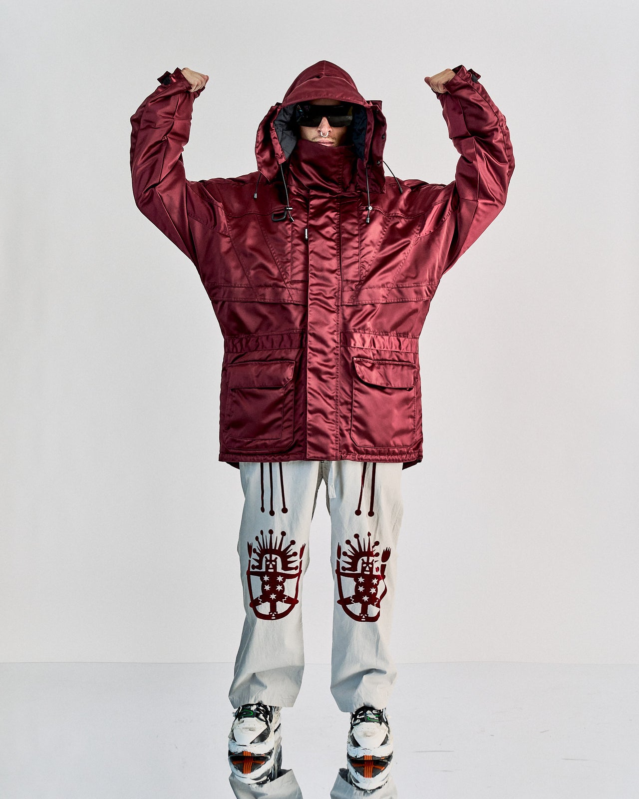 A model in a deep burgundy hooded Balenciaga parka walks confidently against a black background, exuding a sleek and modern winter style.