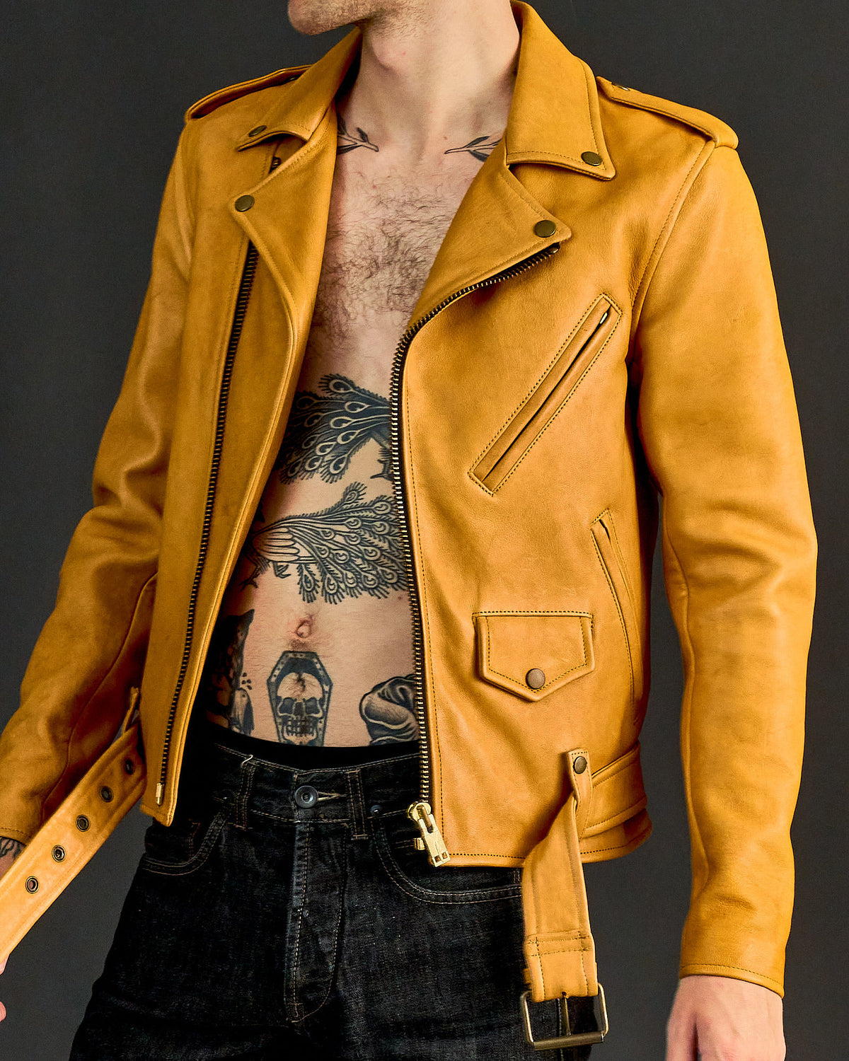 A person wearing a yellow leather Blackmeans biker jacket with a mid-rise design and long sleeves. The jacket features a front buckle detail and appears to be made of soft Japanese cowhide.