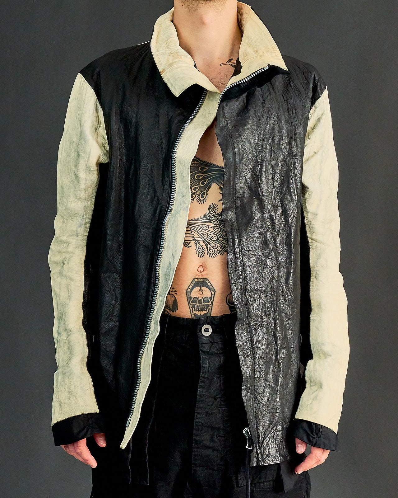 A person wearing a longline zip-up Boris Bidjan Saberi jacket with crumpled buckskin deerhide leather, featuring a double-zip front and a silver-aglet lace detail on the back.