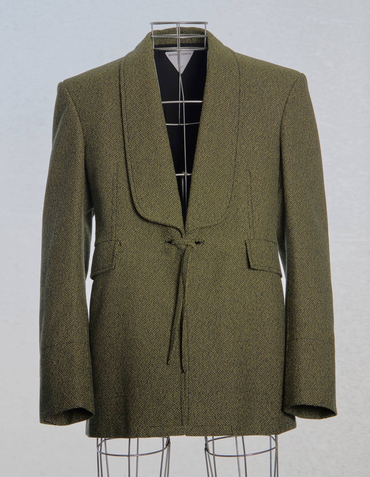 Model walking on a Bottega Veneta runway wearing a green suit with a white bag.