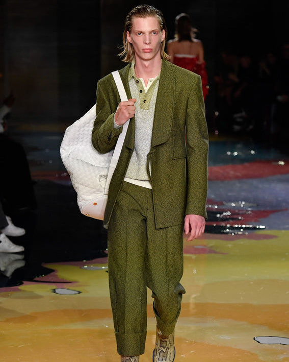 Model walking on a Bottega Veneta runway wearing a green suit with a white bag.