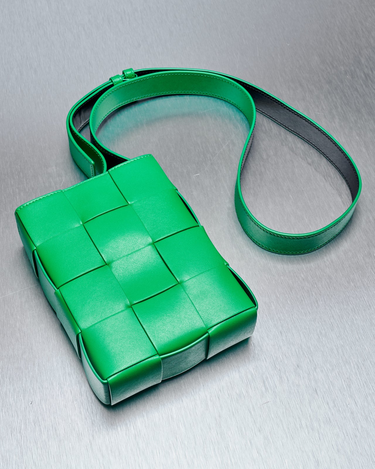 A green woven intrecciato leather shoulder bag with adjustable straps and a magnetic tab closure.