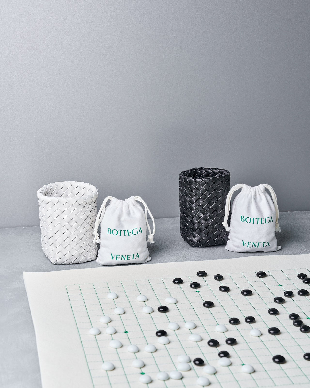 Three Bottega Veneta bags and a Go board with pieces on a gray surface.