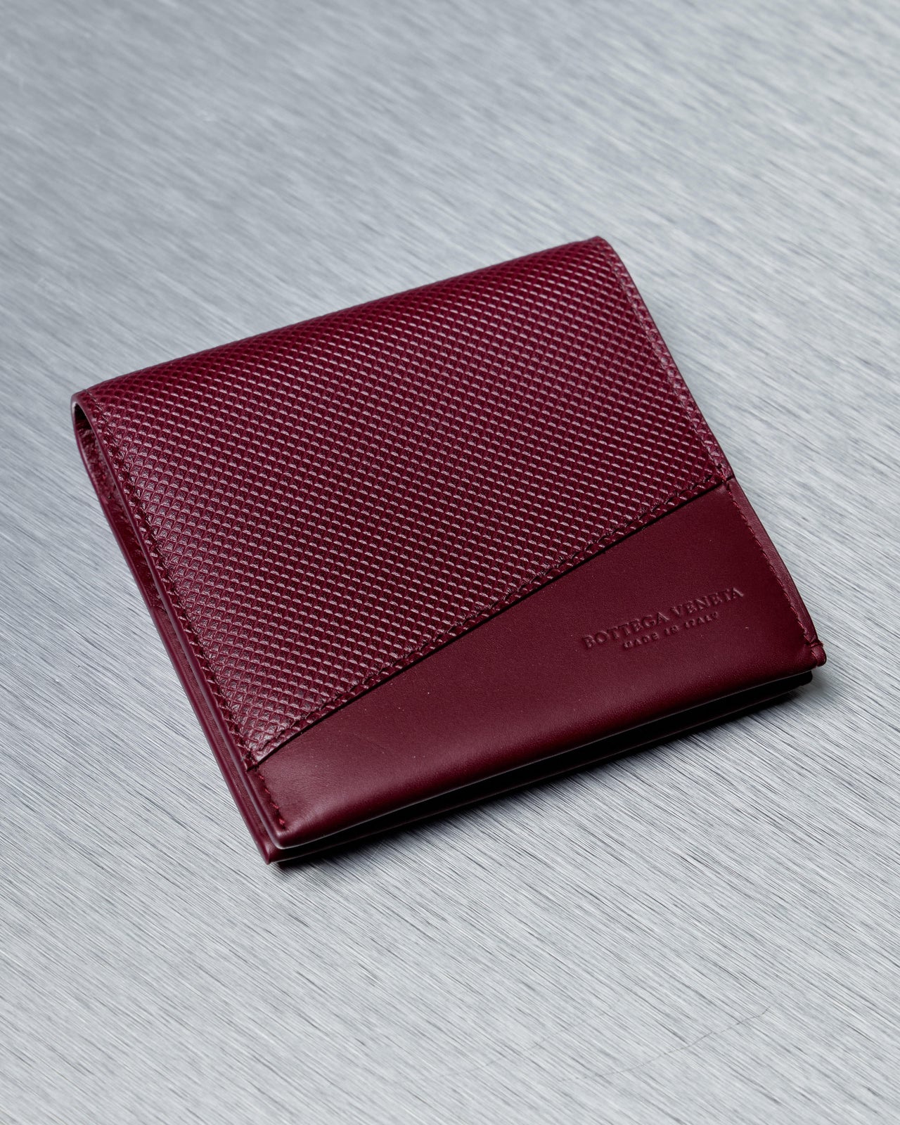 Red leather Bottega Veneta wallet on a gray textured surface