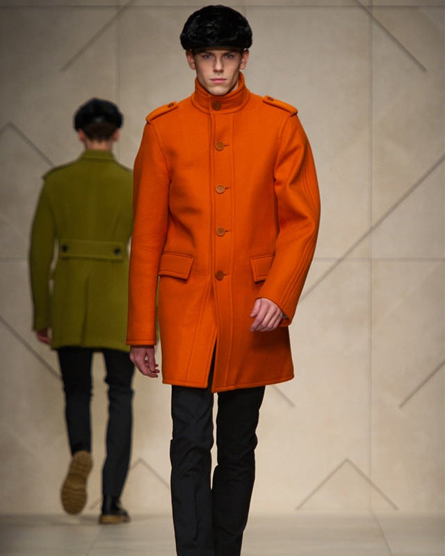 Man wearing an orange Burberry coat walking on a runway with another person in the background.