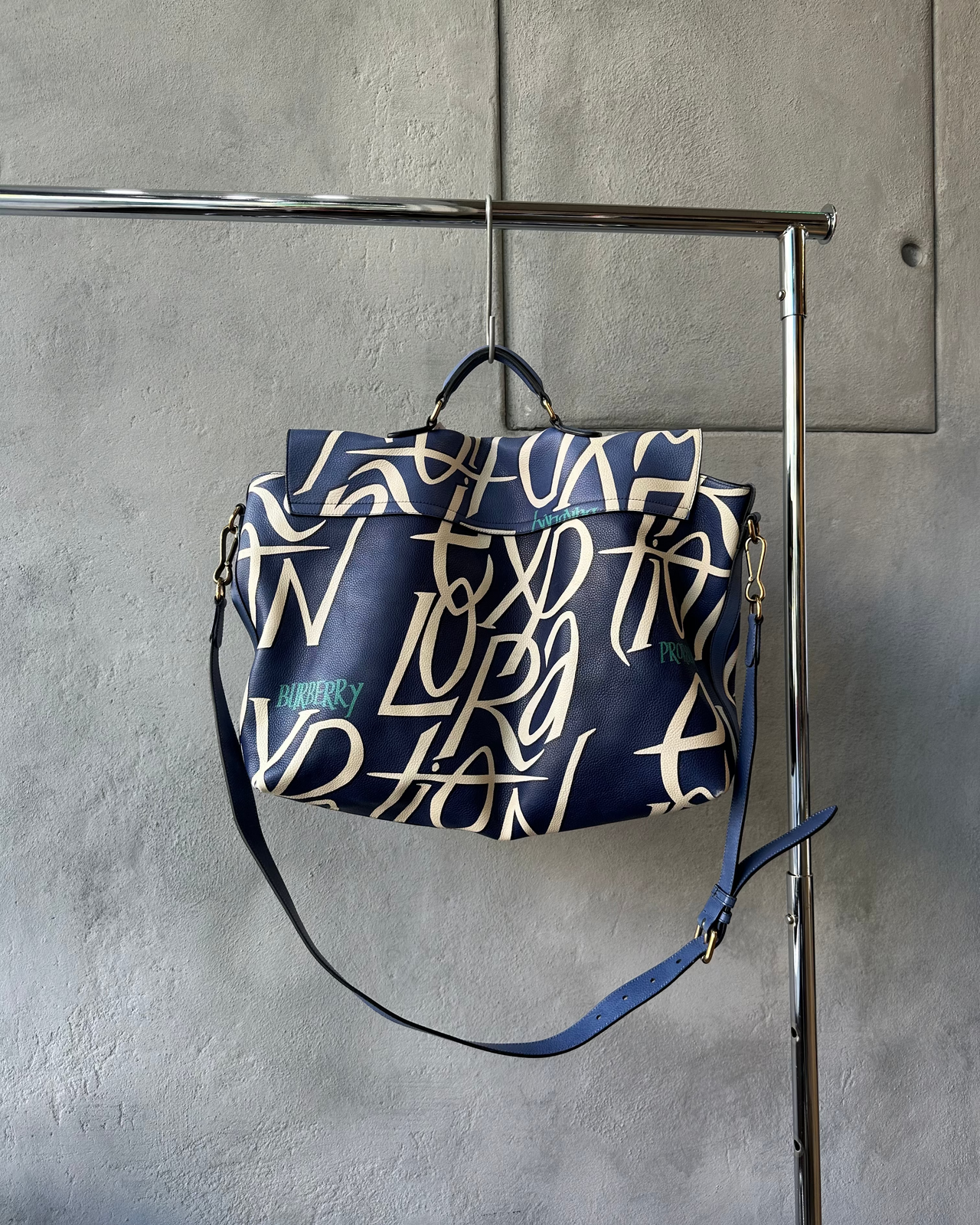 Blue Burberry satchel with white text design on a gray wall background