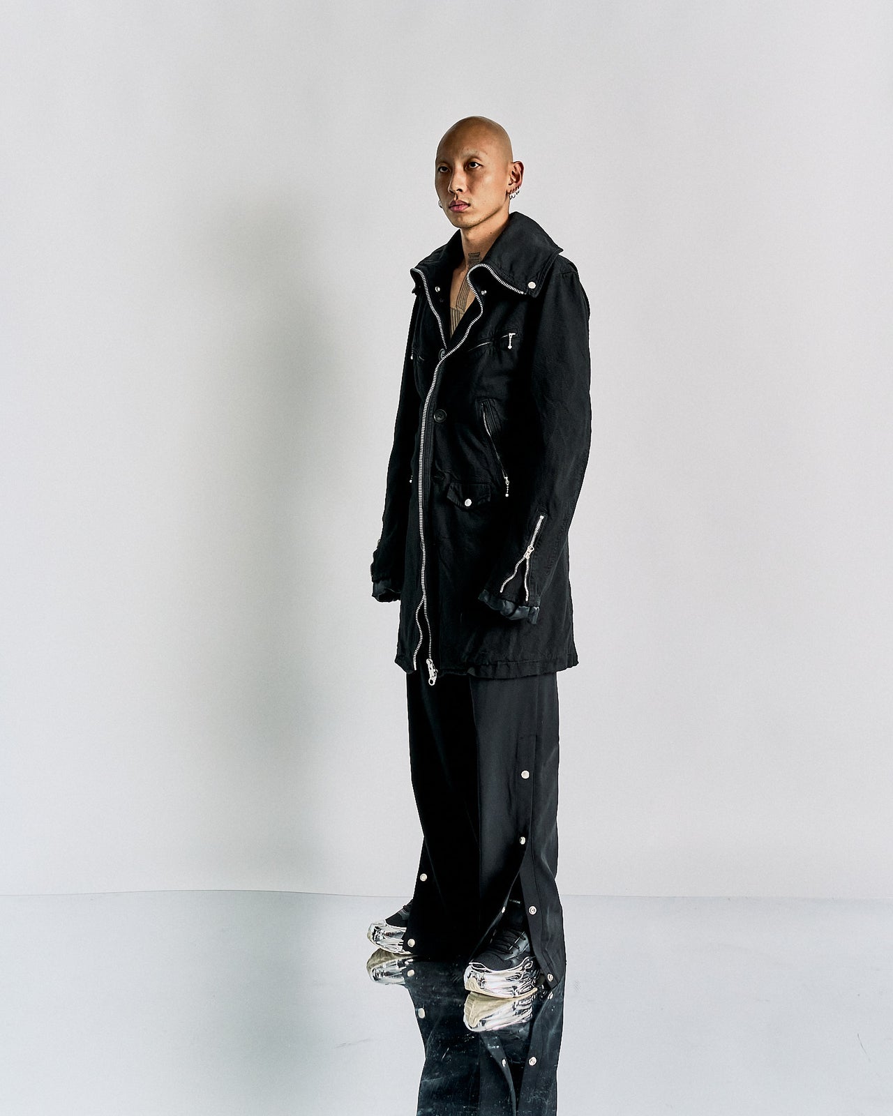 A black longline CDG Junya Watanabe front-zip jacket with collar, featuring external zip and press-stud pockets, and polished hardware.