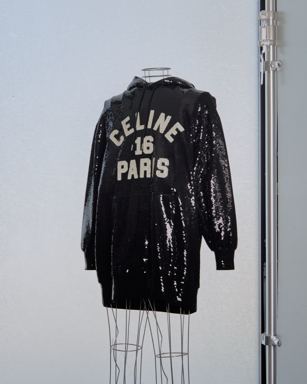 Black sequin hoodie with 'Celine 16 Paris' text on a light blue background