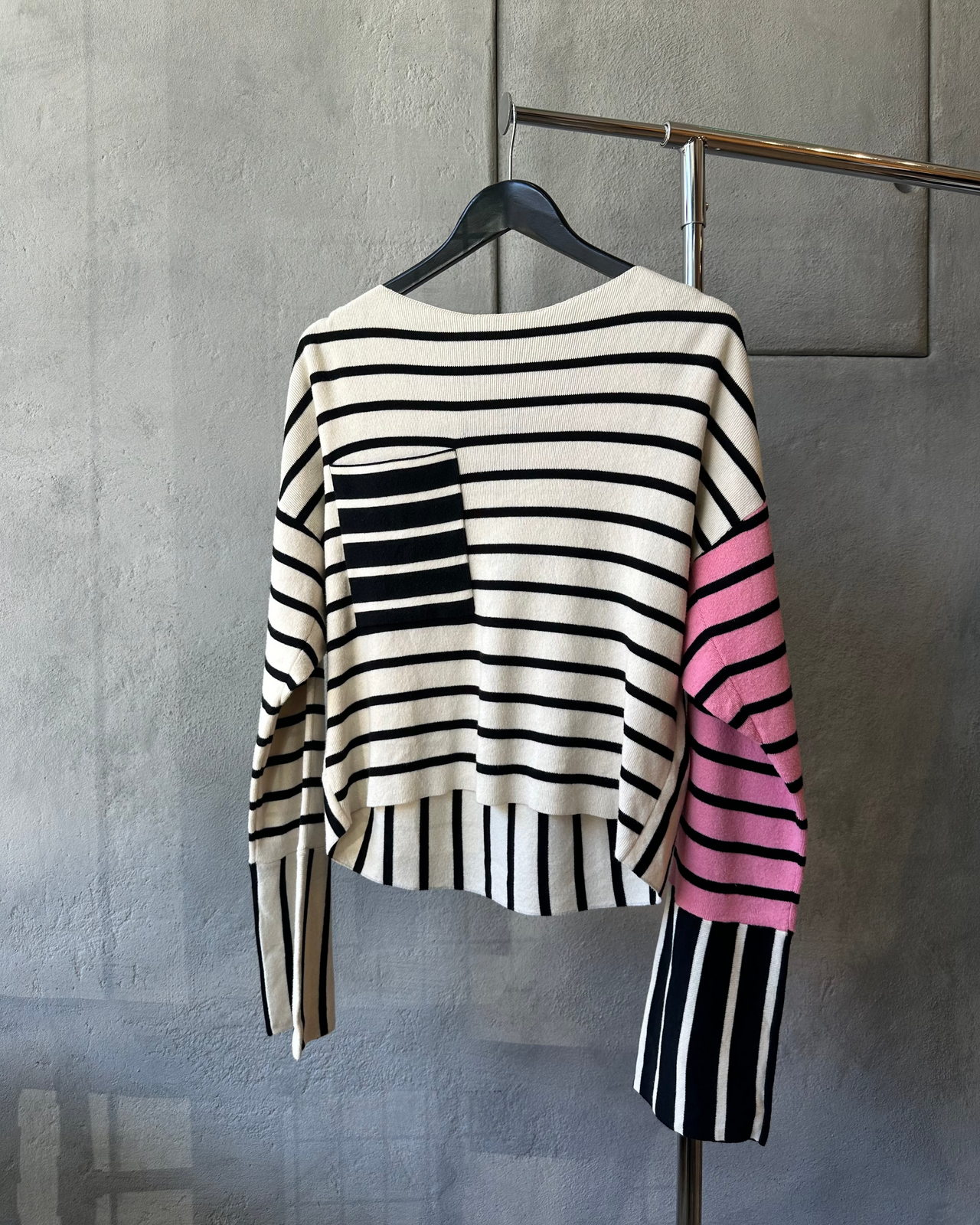 Striped Celine sweater with black, white, and pink colors on a hanger against a gray wall.