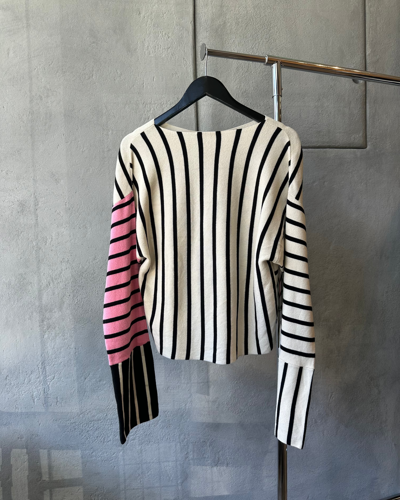 Striped Celine sweater with black, white, and pink colors on a hanger against a gray wall.