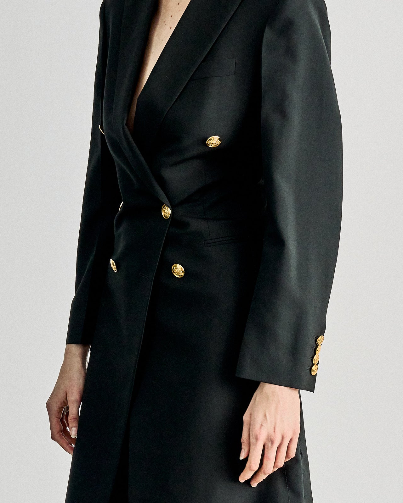 A person wearing a sleek, black double-breasted Celine coat with gold buttons over a long, sheer black skirt and boots, creating a chic, modern look.