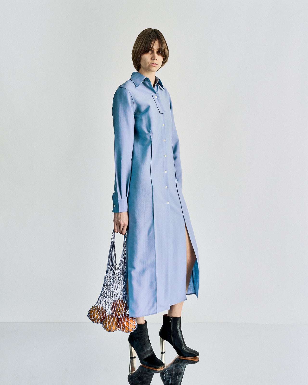 Model on a runway wears a flowing, light blue Celine tunic and pants, holding a black tote. The setting is bright and minimalist, with a neutral-toned background.