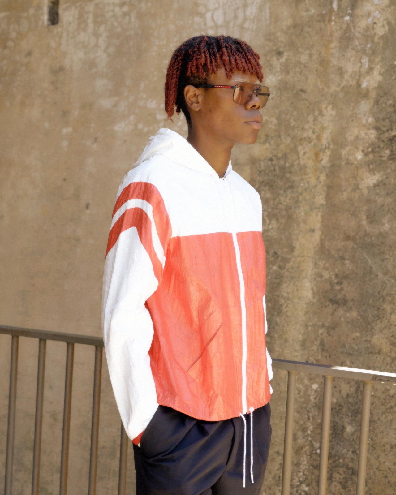 A person wearing a red, white, and black striped hooded Celine windbreaker jacket and black pants.