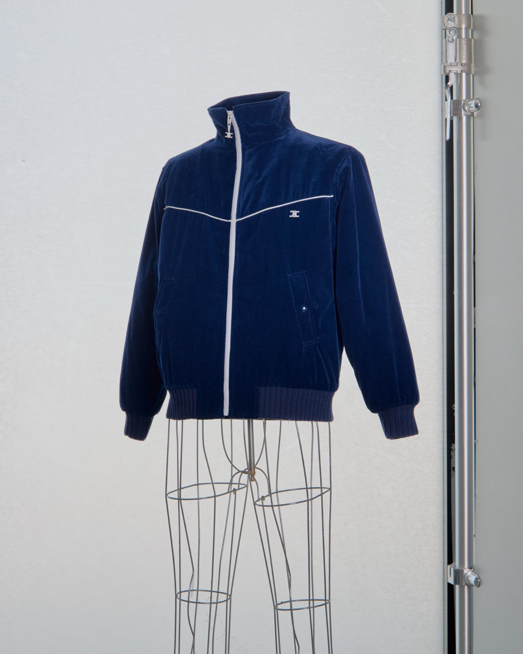 Navy blue Celine jacket with white zipper on a mannequin against a light gray background