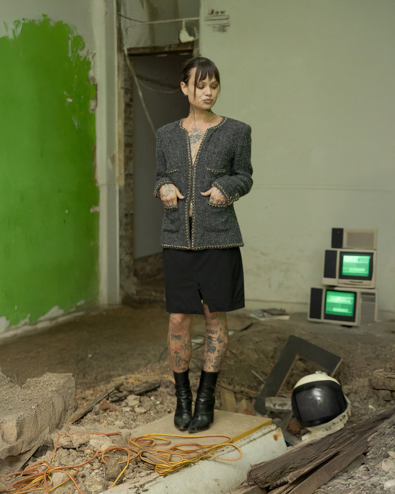 A person stands in a dilapidated room wearing a Chanel 2019 19B Cashmere boucle chain trim jacket, with green walls and debris around.