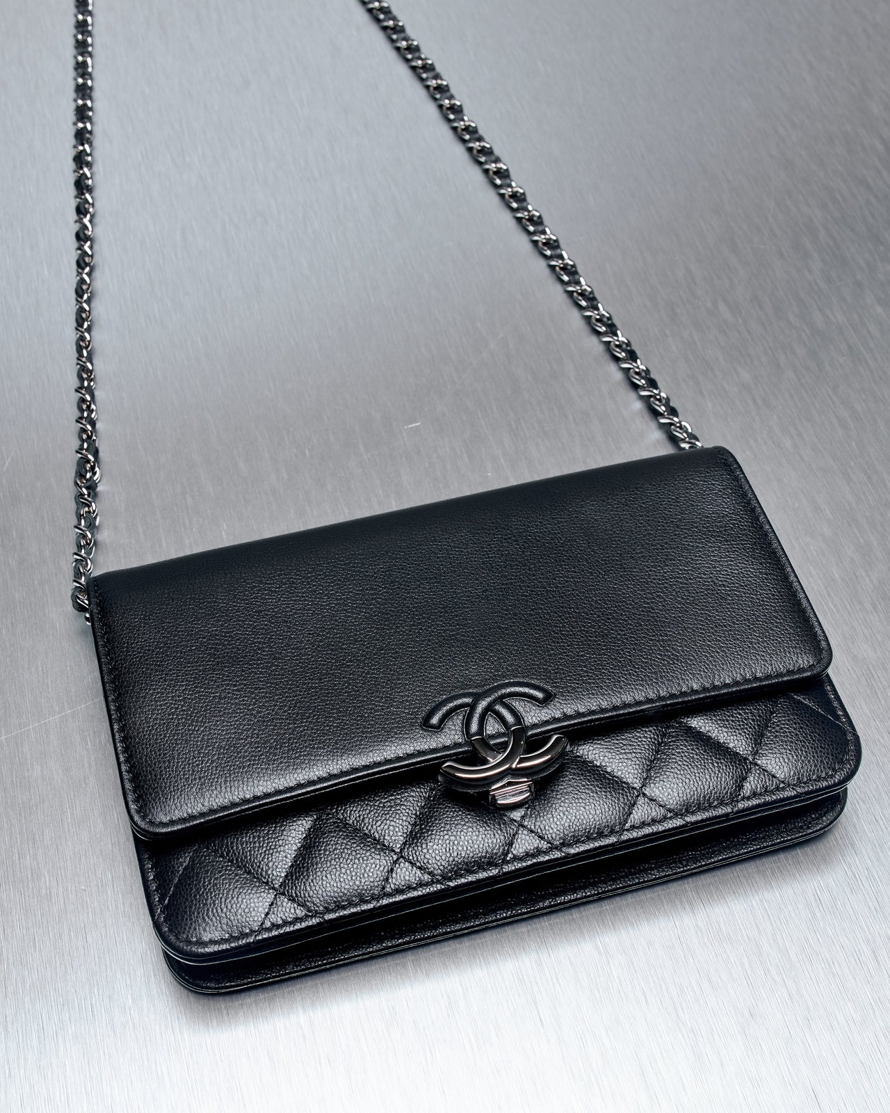 Close-up of a black leather Chanel quilted purse with a silver chain strap and a distinct interlocking CC logo, set on a metal surface.