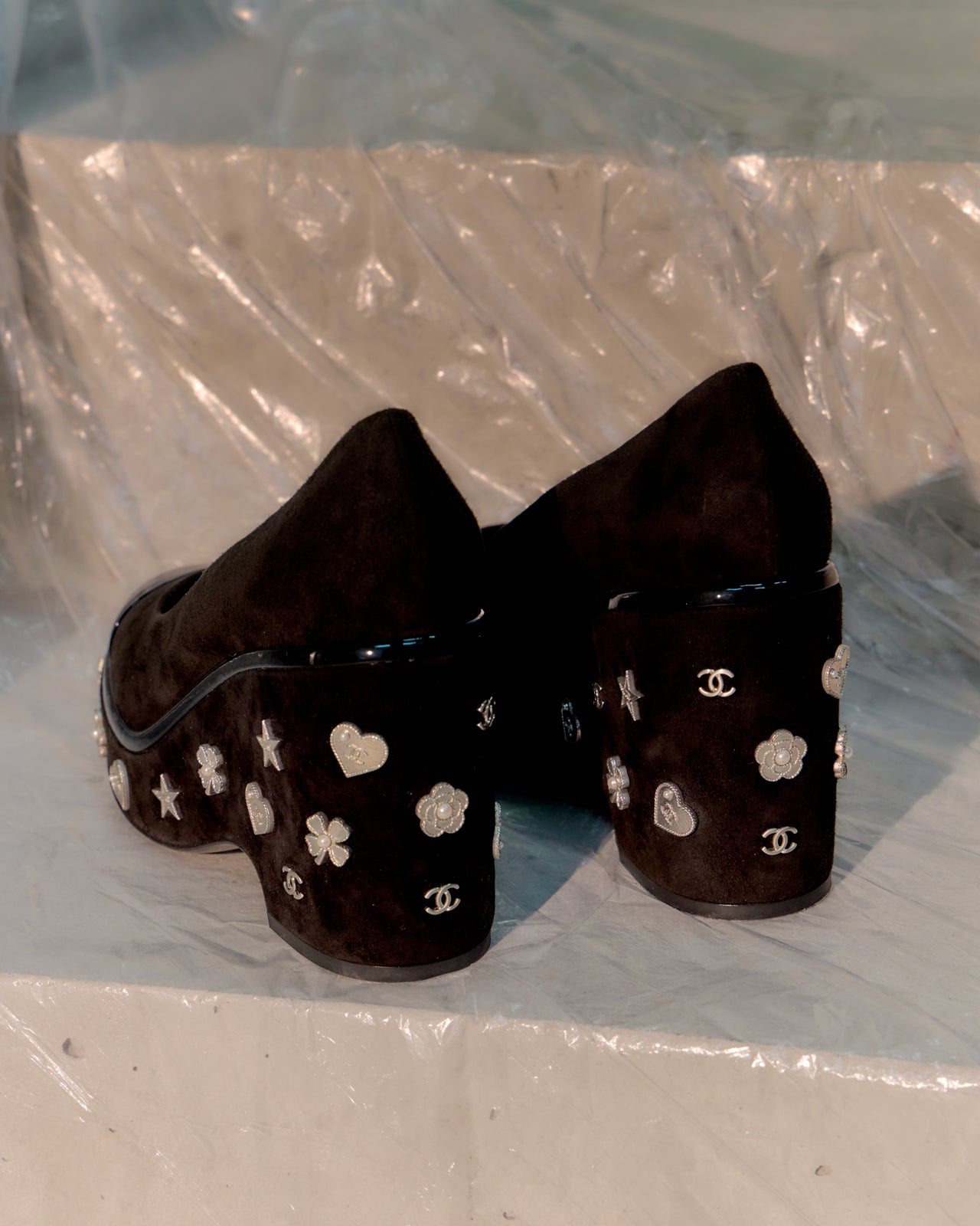 Pair of black high-heeled Chanel shoes with star and clover pattern on a white background