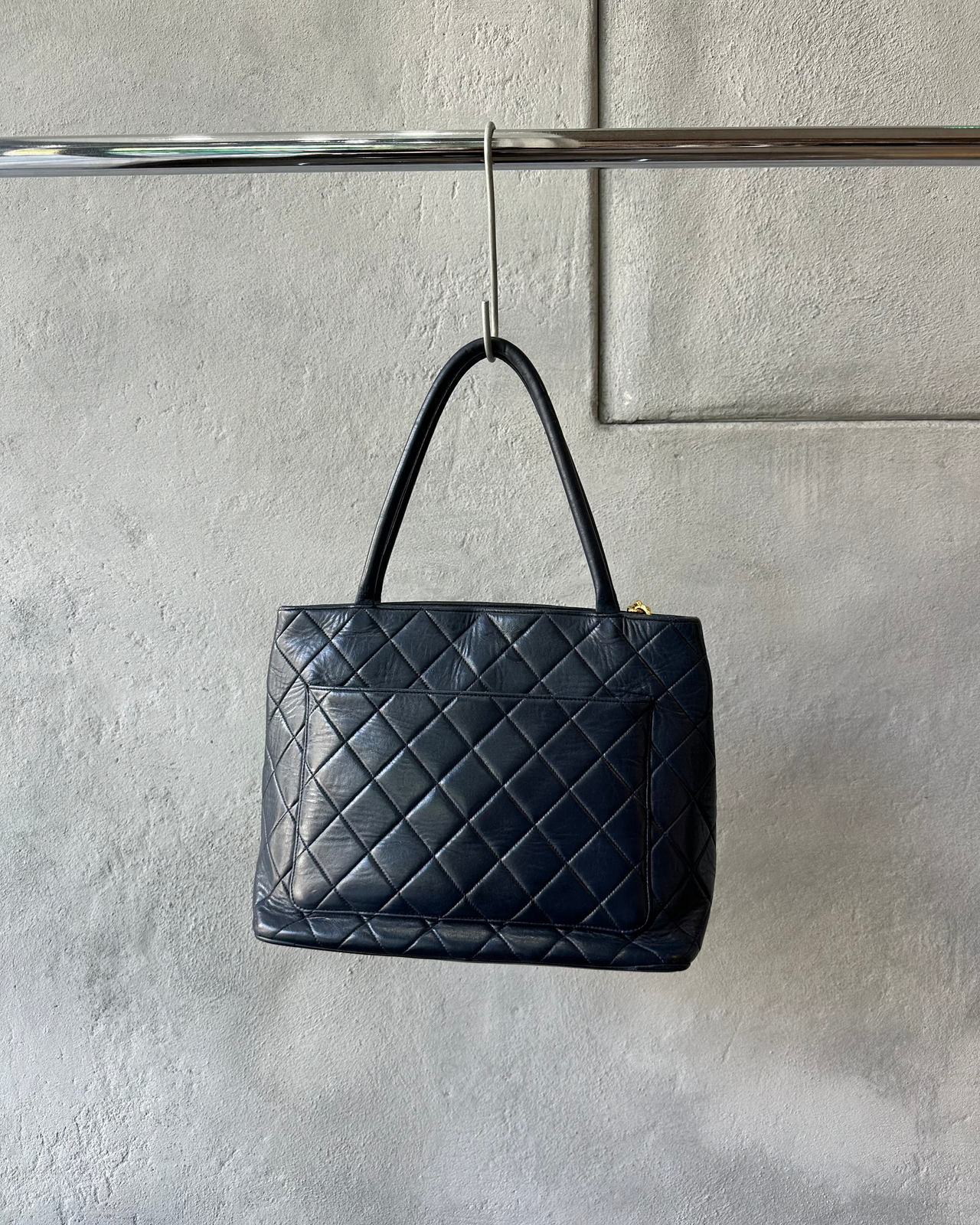 Navy quilted Chanel handbag with a gold clasp on a gray textured background