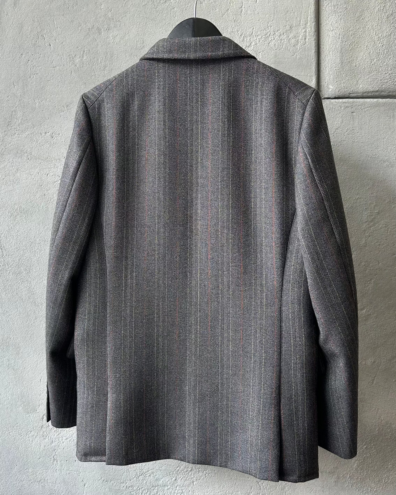 Gray Comme des Garcons Homme Deux blazer on a hanger against a playground background