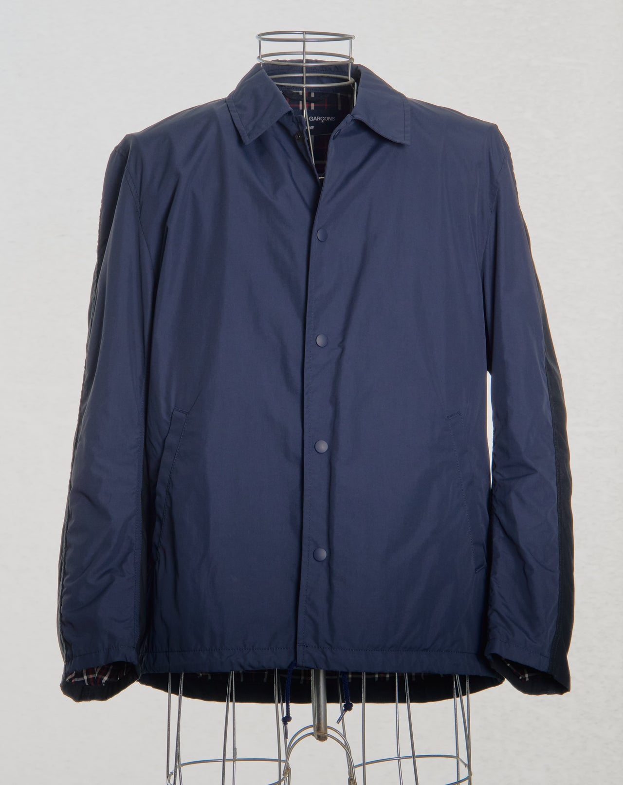 Navy blue Comme des Garcons jacket on a wire rack against a white background