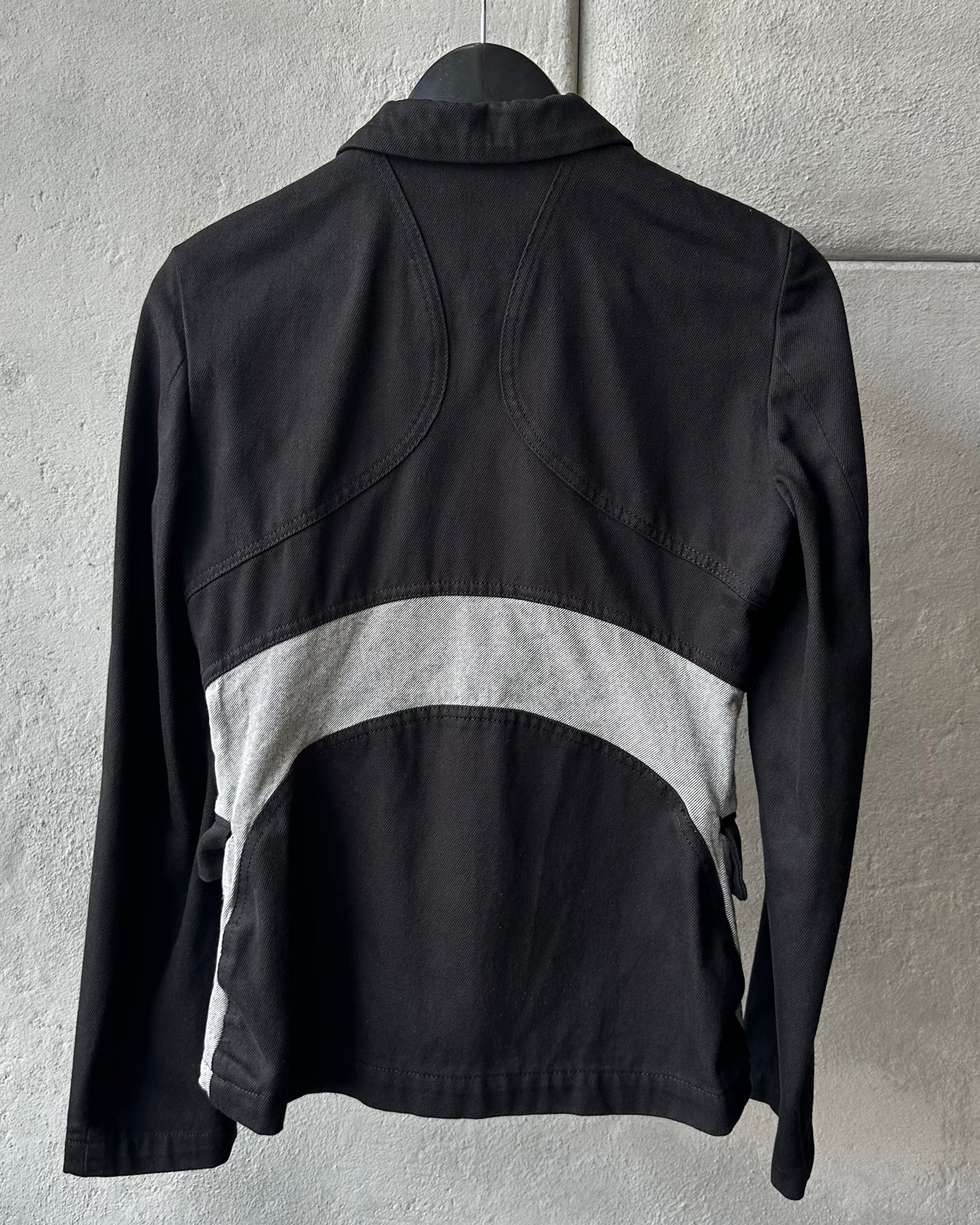 Black Comme des Garcons Homme Plus jacket with gray patchwork design on a hanger against a light gray background