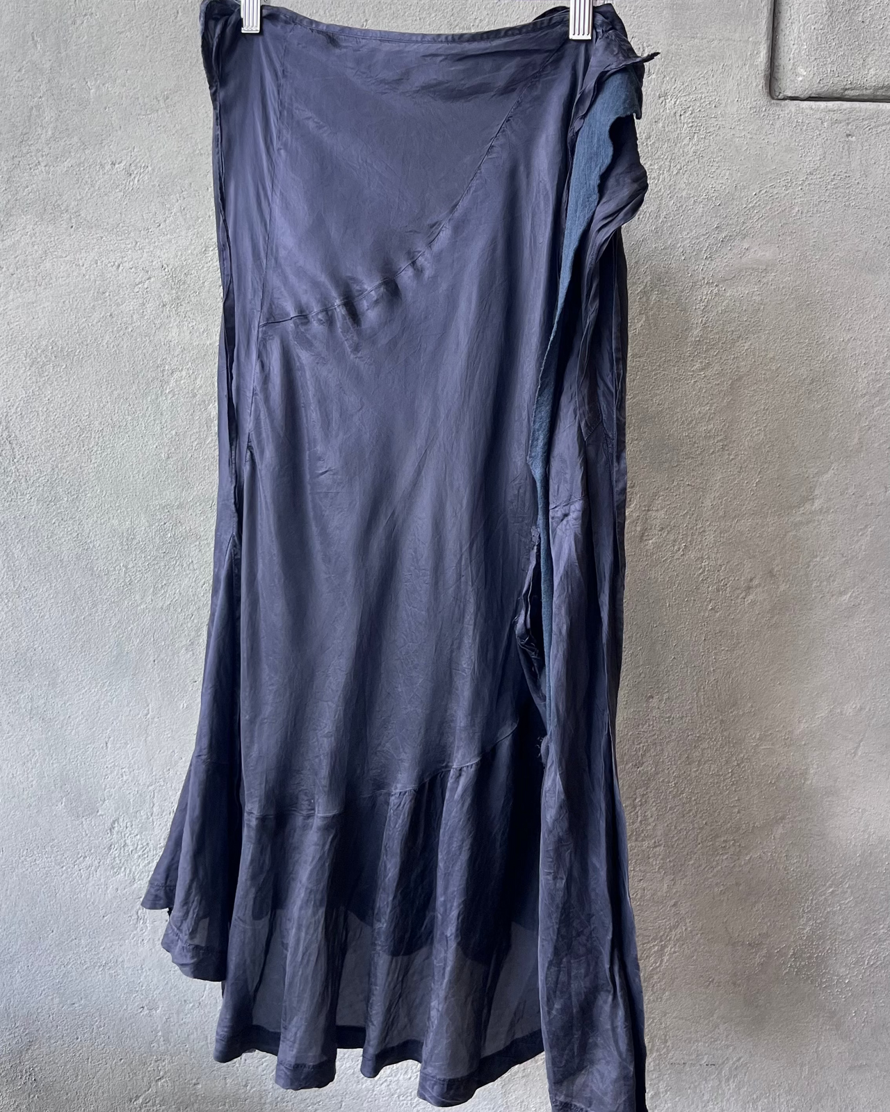 Navy comme des garcons skirt hanging on a rack against a plain wall.