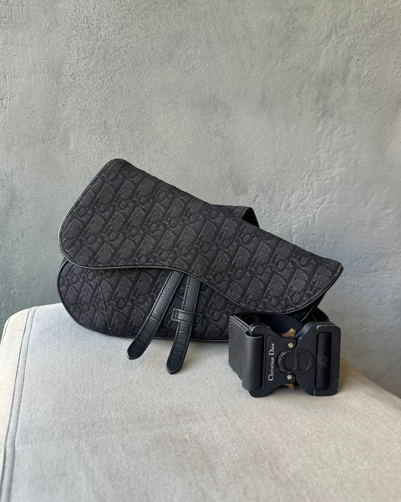 Black Dior harness on a metal stand against a gray tiled wall