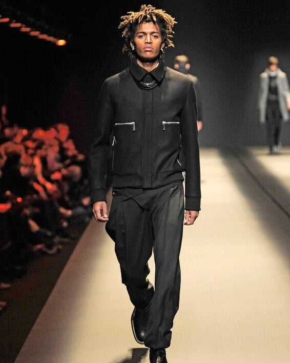 Model walking on a Dior runway wearing a black outfit with reflective accents.